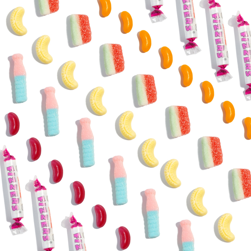 Assorted colourful sweets including bananas, lollipops, and jelly beans on a white background